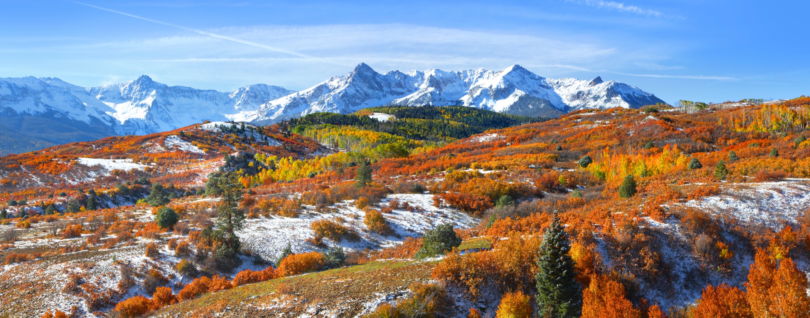 Snow-dusted Colorado peaks above rolling hills of orange and gold autumn aspen